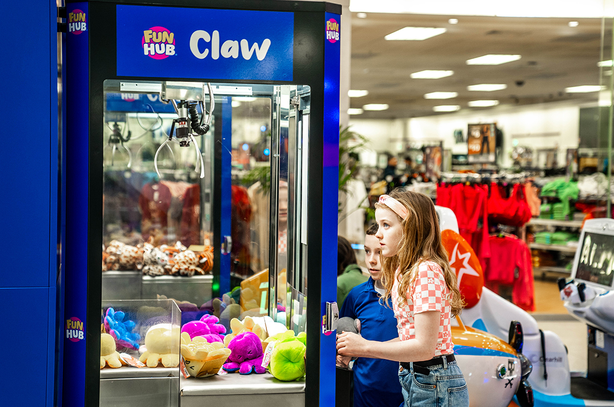Crianças brincando em uma máquina de pelúcias FUN HUB Claw em um shopping